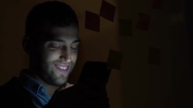 Genç adam cep telefonuyla geceleri karanlık ofisinde