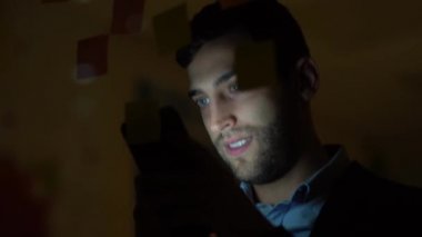 Genç adam cep telefonuyla geceleri karanlık ofisinde