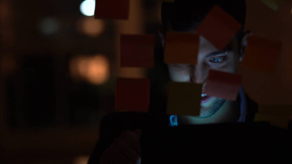 Молодой человек использует мобильный телефон ночью в темном офисе
