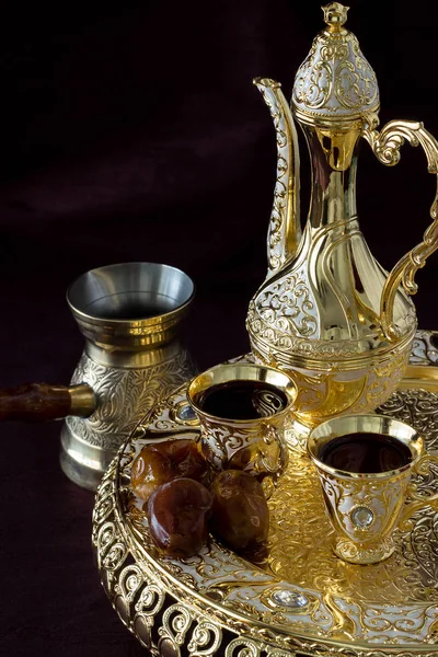 Traditional golden Arabic coffee set with dallah, coffee pot and dates. Dark background