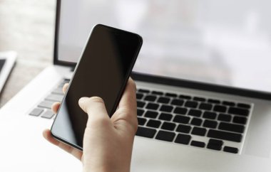 Modern dizüstü bilgisayara karşı kopyalama alanı olan gri renkli akıllı telefonu kullanarak ve tutarak elinizi kapatın. mobil ödeme, çevrimiçi alışveriş kavramı