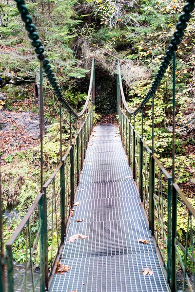 Diminishing perspective of metal suspension footbridge over rive — Stock Photo, Image