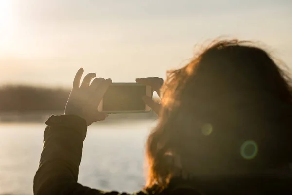 用手机拍摄太阳的年轻妇女。人们享受 — 图库照片