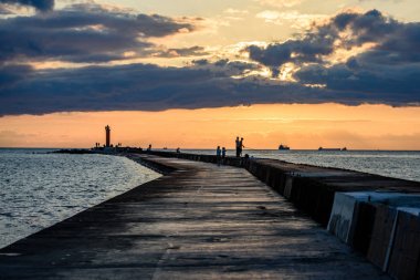 people enjoying sunset on the breakwater in the sea with lightho clipart