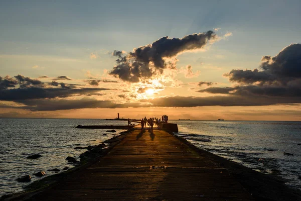 People enjoying sunset on the breakwater in the sea with lightho — Stock Photo, Image