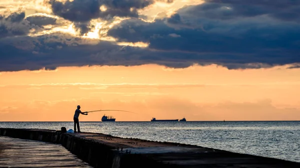 Люди насолоджуються заходом сонця на пробитій воді в морі з маяком — стокове фото