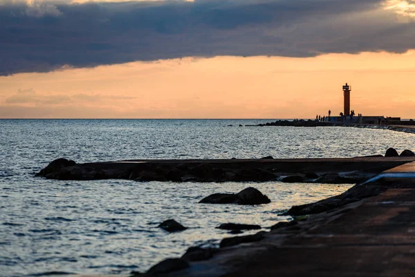 Люди насолоджуються заходом сонця на пробитій воді в морі з маяком — стокове фото