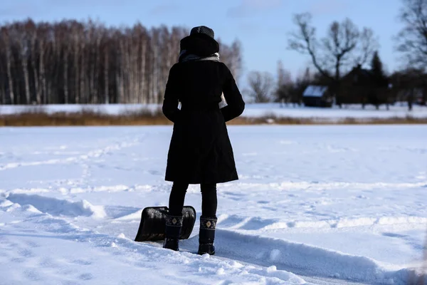Giovane donna in cappotto nero pulizia ghiaccio dalla neve — Foto Stock