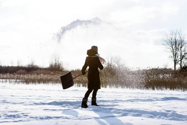 Giovane donna in cappotto nero pulizia ghiaccio dalla neve. lancio di neve — Foto Stock