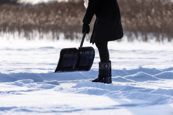 Giovane donna in cappotto nero pulizia ghiaccio dalla neve — Foto Stock