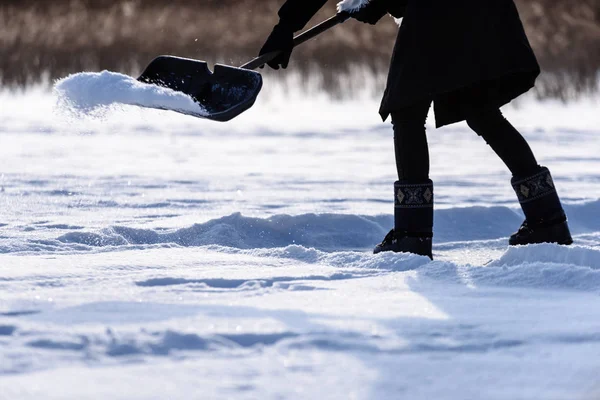 Молода жінка в чорному пальто очищає лід від снігу — стокове фото