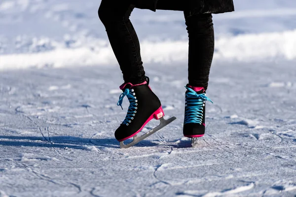 Jeune femme en manteau noir patinant sur le lac gelé dans la neige — Photo