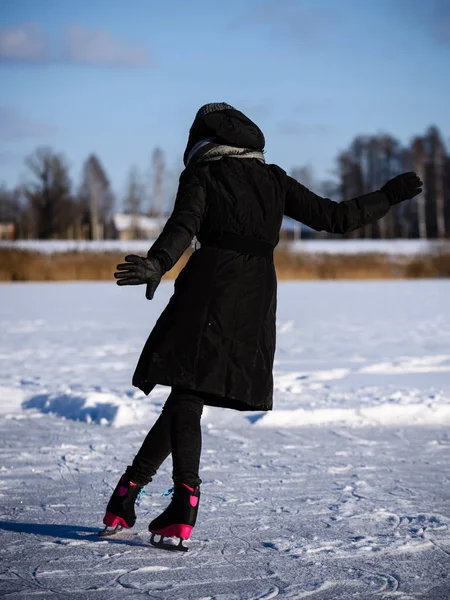 Giovane donna in cappotto nero pattinaggio sul lago ghiacciato nella neve, le — Foto Stock