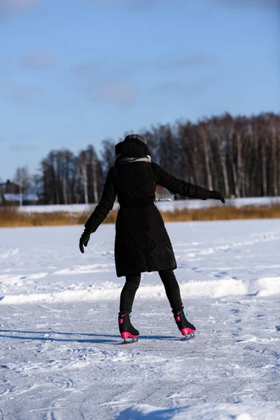 Fiatal nő fekete kabátot, korcsolyázás a befagyott tavon a hóban, le — Stock Fotó