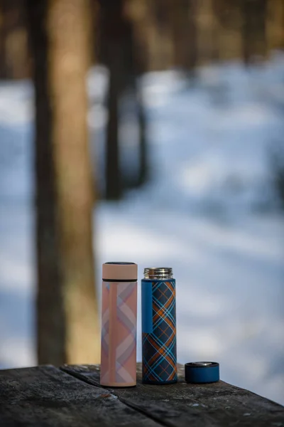 Thermoses colorées sur table en bois dans la forêt d'hiver — Photo