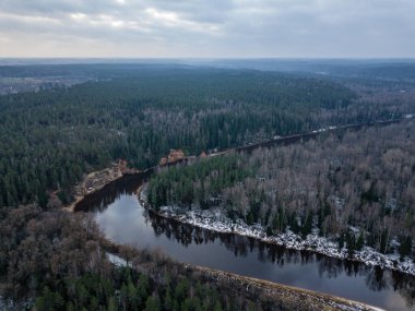 Kış ormanındaki nehirde yukarıdan yeşil ağaçlar var. Letonya 'daki Gauja nehrinin hava aracı görüntüsü.