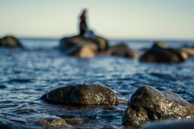 Kumsalda mavi su ve kumda büyük kayalar olan güneşli bir sahil. Letonya açık gökyüzü altında