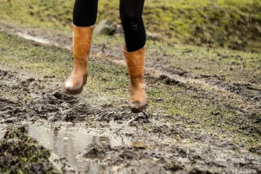 Sonbaharda çamur birikintisinde turuncu lastik çizmelerle zıplayan kadın.