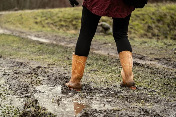 woman jumping in the puddle of mud in autumn with orange rubber boots