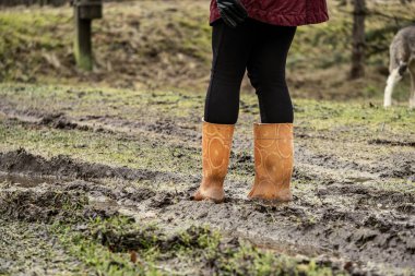 Sonbaharda çamur birikintisinde turuncu lastik çizmelerle zıplayan kadın.