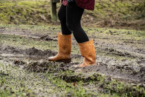 Sonbaharda çamur birikintisinde turuncu lastik çizmelerle zıplayan kadın.
