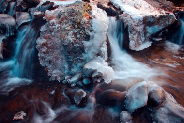 Donmuş dağ nehri, donmuş bir dağ nehrinin buzlu kayaların arasından akması. .