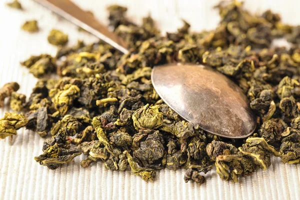 Dry leaves of green tea and teaspoon