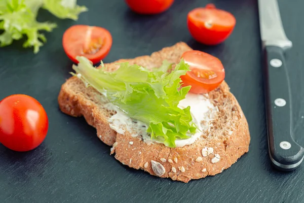 Pasul de a face un sandwich cu salată verde și roșii: roșii cherry, frunze verzi, pâine și un cuțit pe placa de bucătărie . — Fotografie, imagine de stoc