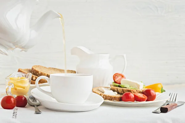 Déjeuner avec des légumes frais, un ensemble blanc, le thé est versé d'une théière dans une tasse . — Photo