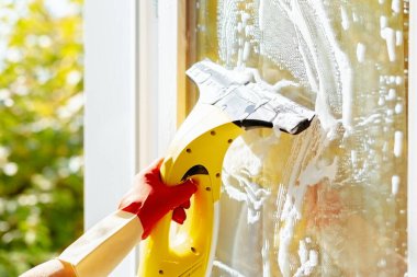 Lastik eldivenli bir kadın eli, silecekle pencereyi temizler.