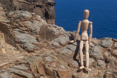 Tahta adam okyanusa karşı kayalıklarda dinlenmek için çömeldi..