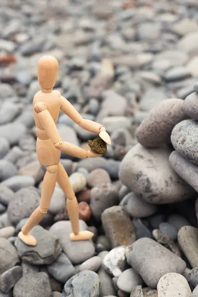 De figuur van een houten man bouwt een piramide van stenen op het strand. — Stockfoto