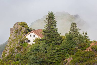 Dağlarda bulutların arasında fayanslı çatısı olan beyaz bir ev..