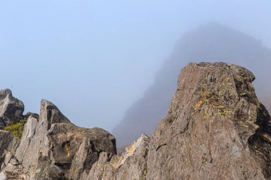 Siste ve mavi gökyüzünde, dağların tepelerinde taş uçurumlar var..