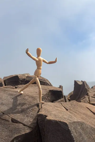 De gestalte van een houten man springend op rotsen in de bergen. — Stockfoto