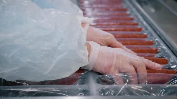 Le travailleur emballe des saucisses fumées sur une chaîne d'emballage semi-automatique . — Video