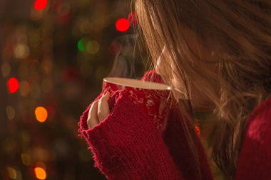 Elinde bir fincan sıcak çikolata, çay ya da Noel ağacının önünde kahve olan genç bir kadın. Rahatlatıcı ve noel konsepti.