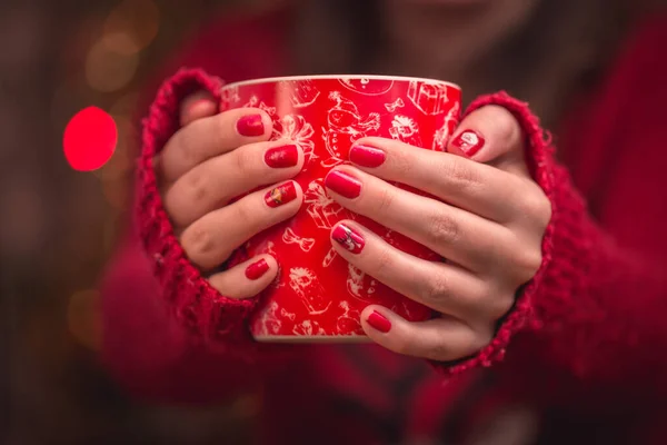 Kobiety trzymają czerwoną filiżankę kawy. Z pięknym zimowym manicure. — Zdjęcie stockowe