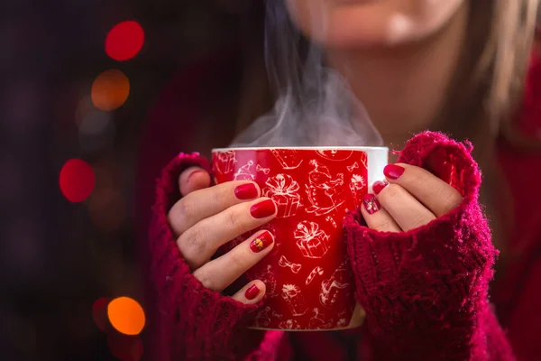 Dettaglio di mani di donna che tengono calda una tazza di tè con vapore. Sfocatura sfondo di Natale. Concetto Natale o inverno . — Foto Stock