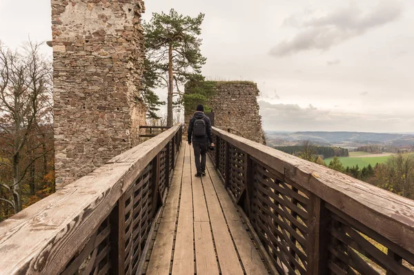 Hombre fotógrafo turístico sosteniendo la cámara caminando sobre un viejo puente de madera en otoño. Puente de madera y antiguo castillo . —  Fotos de Stock