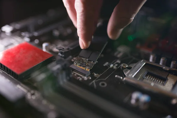 Focus at SSD slot, type M.2 with support for NVMe, on computer motherboard. Technician is installing new fast high capacity drive with flash chips, known as SSD. — Stock Photo, Image