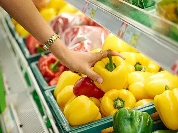 Woman choosing yellow sweet pepper in store