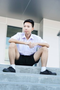 Beton zeminde oturan yakışıklı Taylandlı üniformalı öğrenci.