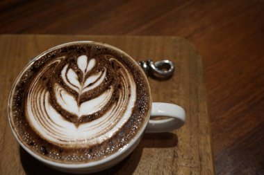 Beyaz fincanda kahve ve ahşap masada kahve sanatı.