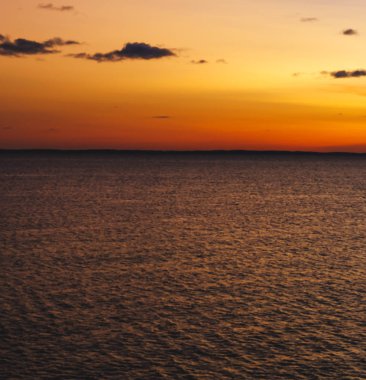 Denizde gün batımı. Gökyüzü, batan güneşin aydınlattığı bulutlarla