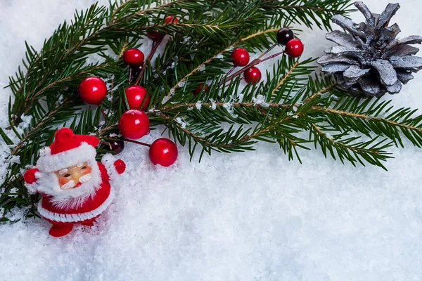 Figurka Santa Claus na pozadí zelené smrkové větve holly bobule. — Stock fotografie