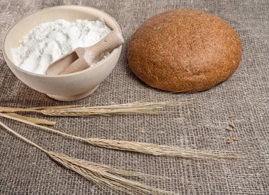 Pişmiş ekmek, bir kase un ve bir demet buğday çerçevede bir çuval bezi