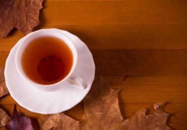 Ahşap bir masaya fincan çay ve sonbahar yaprakları.