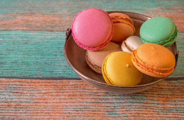 Eski bir ahşap zemin üzerinde metal bir fincan macarons