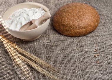 Pişmiş ekmek, bir kase un ve bir demet buğday çerçevede bir çuval bezi